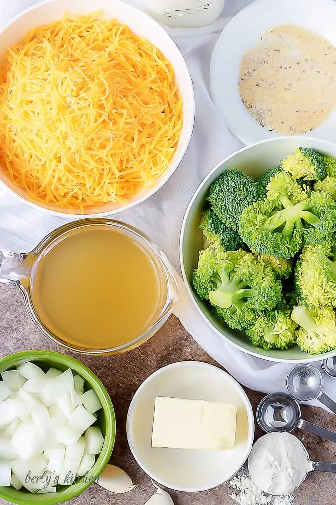 Ariel view of broccoli, cheese, broth, butter, onions, garlic, seasonings, and flour used for broccoli cheese soup.
