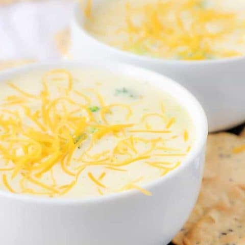 Two bowls of broccoli cheese soup covered in shredded cheddar cheese.