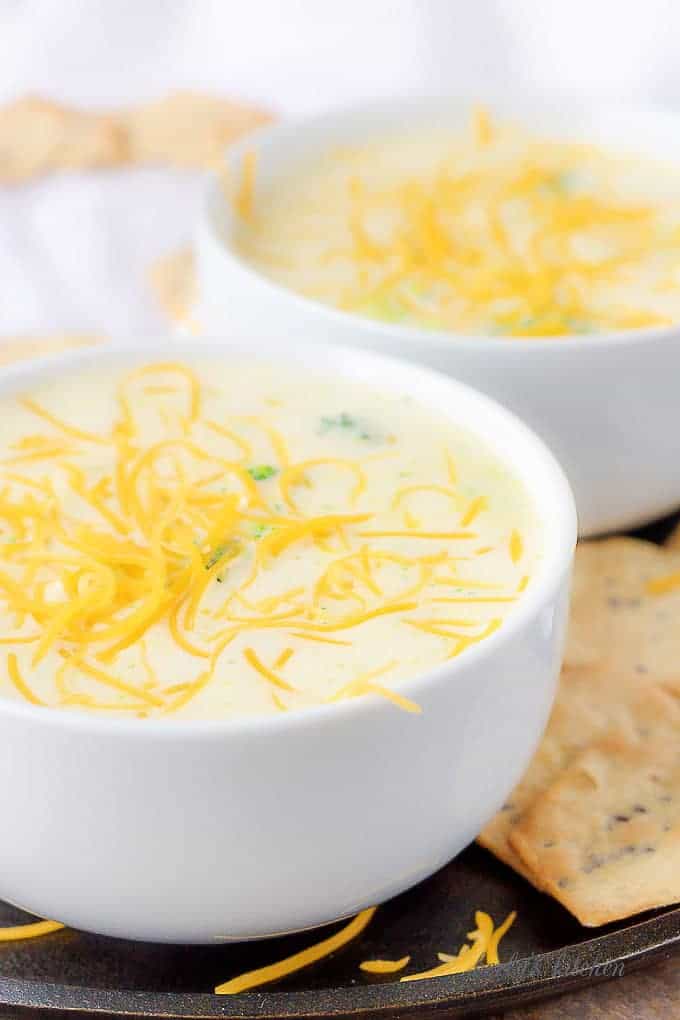Two bowls of broccoli cheese soup covered in shredded cheddar cheese.