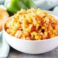 A white bowl of Mexican rice surrounded by fresh bell peppers and onions.