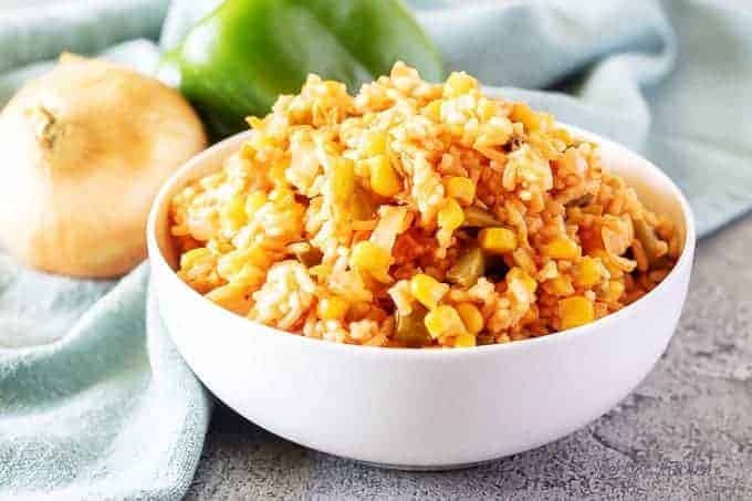 A white bowl of Mexican rice surrounded by fresh bell peppers and onions.