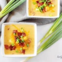 An aerial view of the potato soup with bacon in square bowls garnished with bacon and green onion.