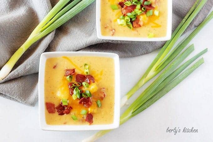 An aerial view of the potato soup with bacon in square bowls garnished with bacon and green onion.