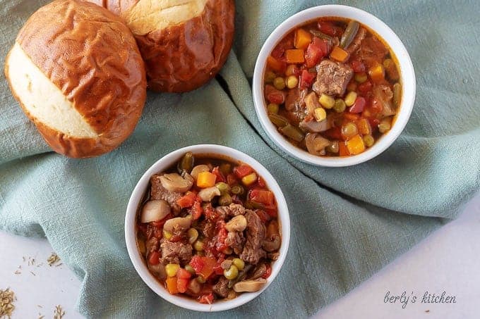 The finished vegetable beef soup in a white bowl and served with a pretzel roll.