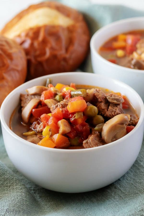 An angled photo of the finished vegetable beef soup in a whit bowl served with a pretzel roll.