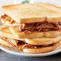 Two stacked pulled pork sandwiches, ready to be served on a white and green plate.
