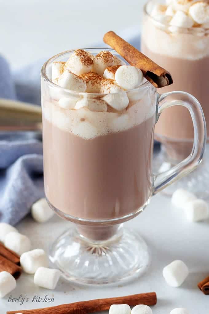 A close-up picture of the spiked hot chocolate in a mug, topped with marshmallows and cinnamon, and garnished with a cinnamon stick.