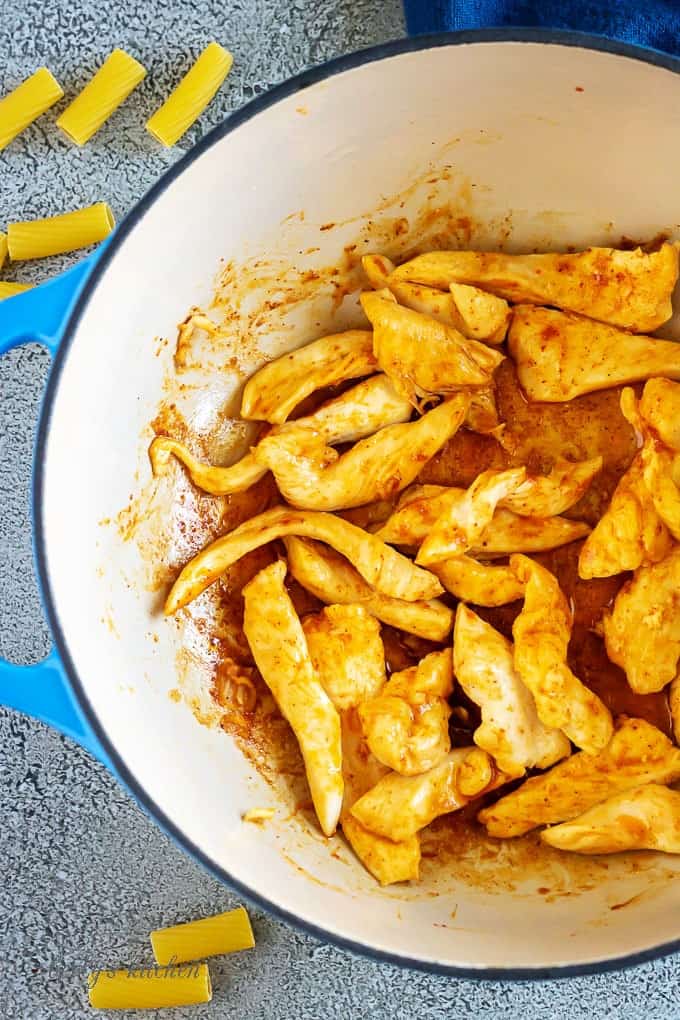 Arial view of seasoned chicken cut into strips in a dutch oven.