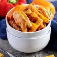 Cheesy chicken fajita pasta in two stacked white bowls with scattered pasta and bell peppers in the background.