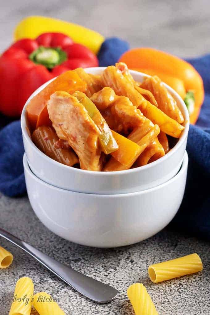 Cheesy chicken fajita pasta in two stacked white bowls with scattered pasta and bell peppers in the background.