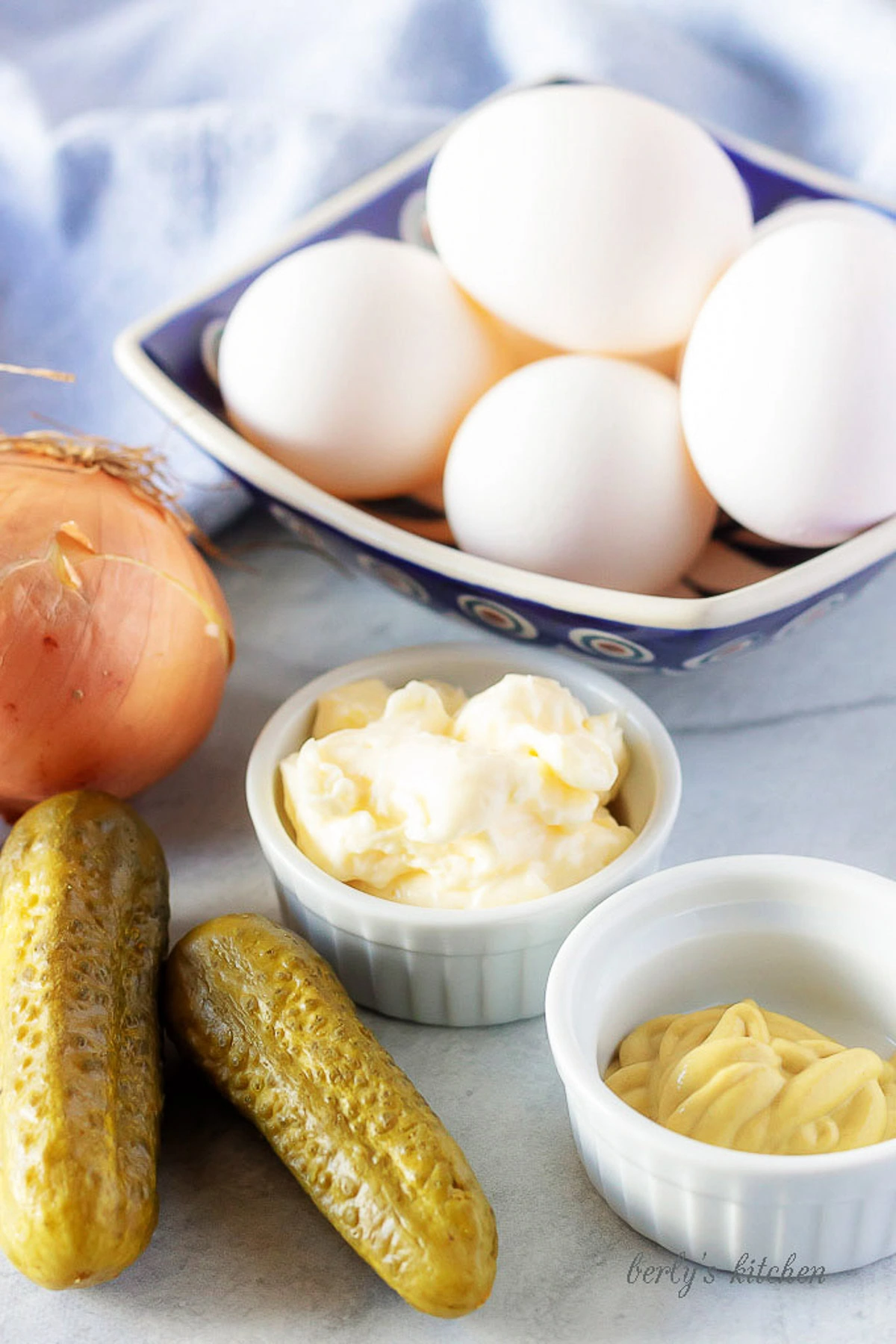 All of the easy deviled eggs ingredients like pickles, mayonnaise, mustard, and white onion in bowl.