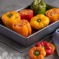 Ground turkey stuffed peppers in a baking dish next to scattered rice and a blue linen.