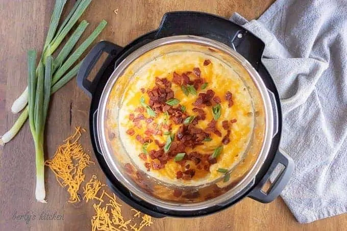 Arial view of loaded mashed potatoes in an Instant Pot next to shredded cheese, scallions, and a blue linen.