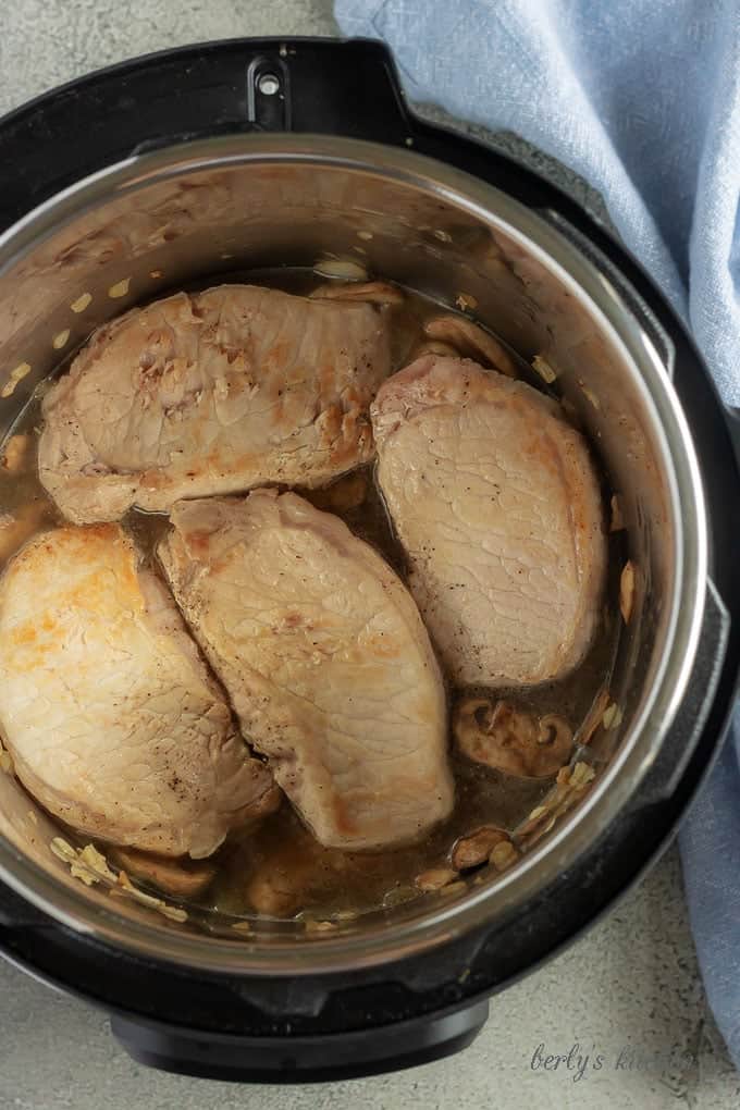 The Instant Pot pork chops being placed back into the pot to finish cooking with the mushrooms.