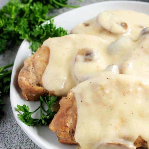 A close-up photo of the instant pot pork chops, covered with gravy and being served on a whit serving platter.