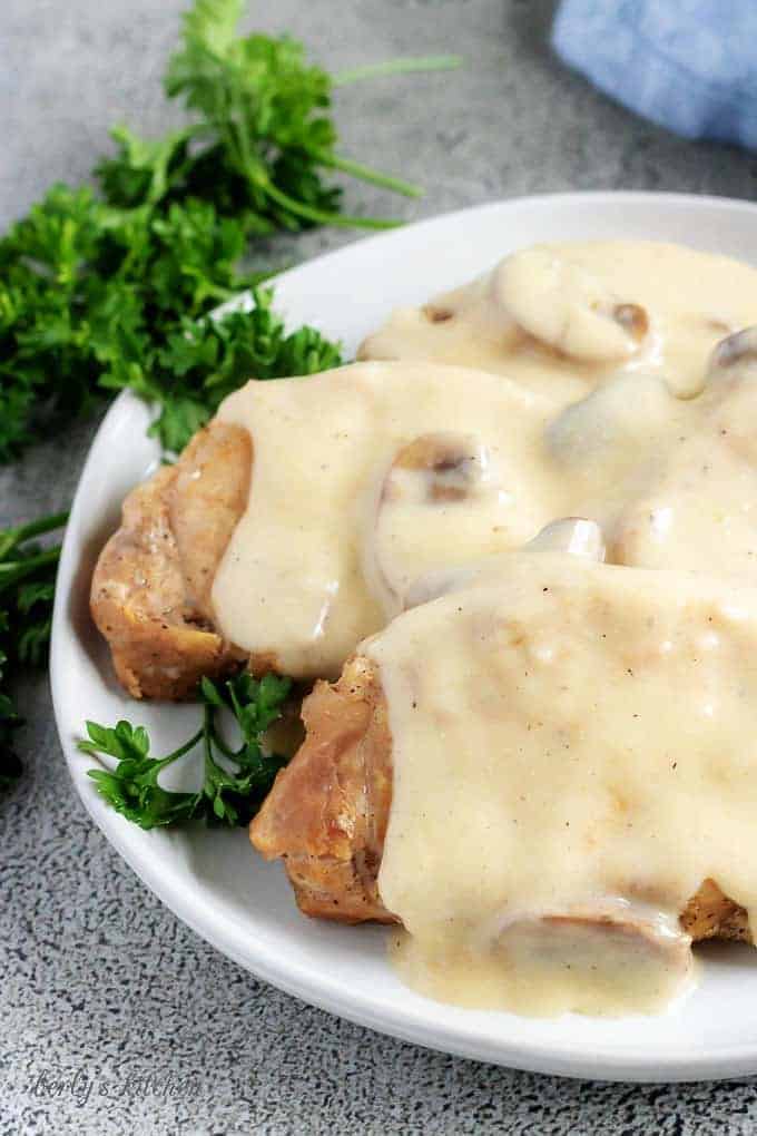 A close-up photo of the Instant Pot pork chops, covered with gravy and being served on a whit serving platter.
