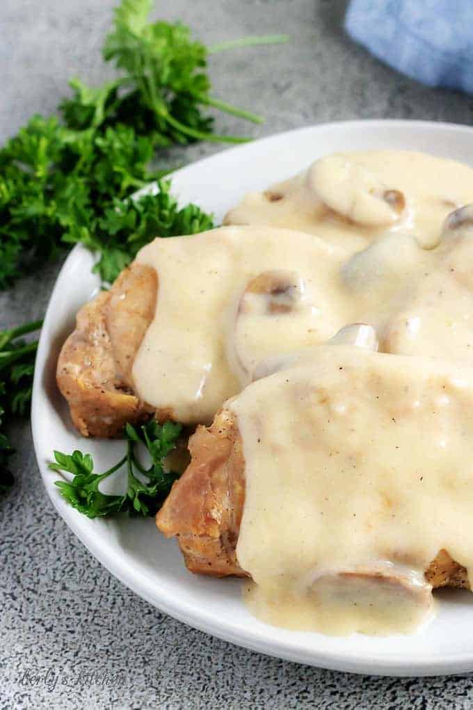 A close-up photo of the instant pot pork chops, covered with gravy and being served on a whit serving platter.