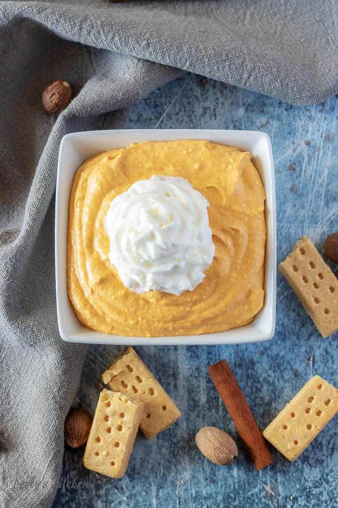 An aerial view of the finished pumpkin dip in a square bowl, topped with ready whip.