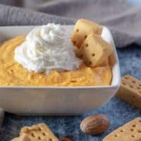 The finished pumpkin dip, in a square serving bowl, topped with whipped cream.