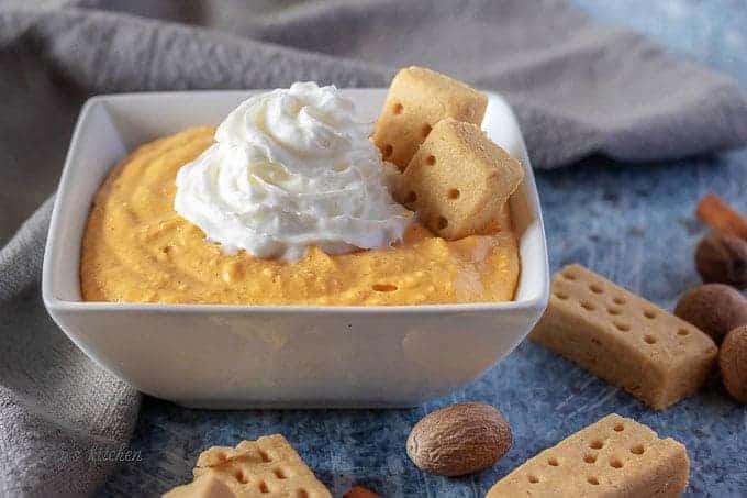 The finished pumpkin dip, in a square serving bowl, topped with whipped cream.