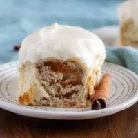 A close-up photo of the finished pumpkin pie cinnamon rolls topped with a thick maple cream cheese frosting.
