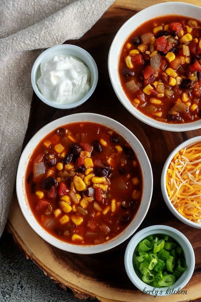 A close-up photo of the finished black bean chili, served in white bowls, sitting on a wooden decorative tray.