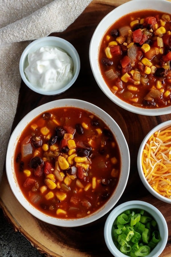 The picture is of the finished black bean chili, served in white bowls with sides of green onions, cheese, and sour cream as toppings.