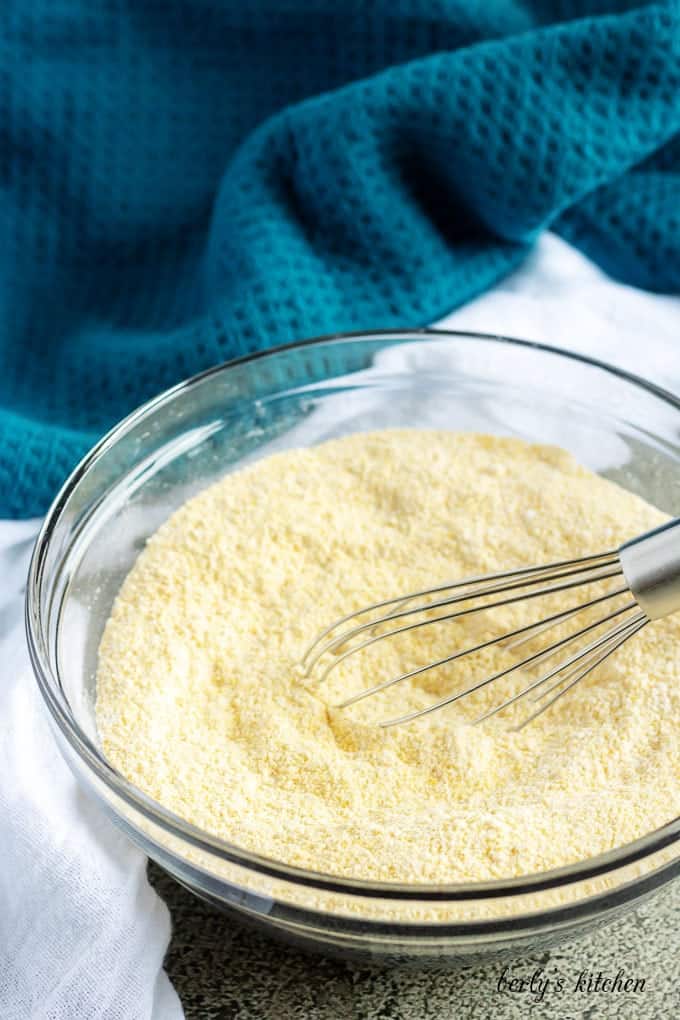 Flour, cornmeal, baking powder, and salt mixed together in a glass bowl for buttermilk cornbread. 