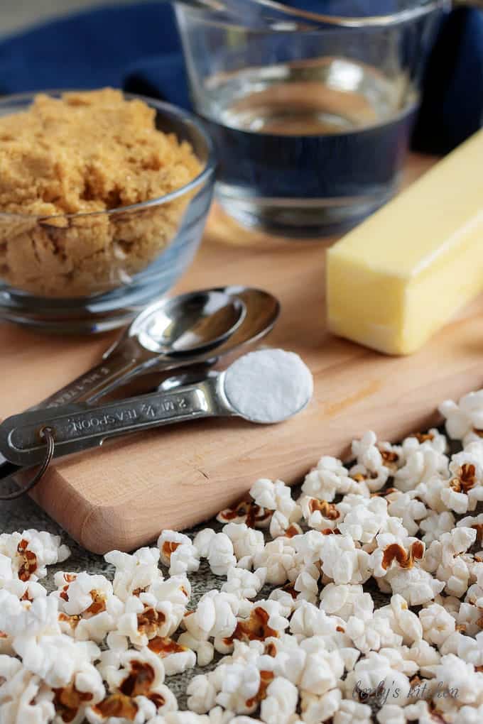 The caramel corn ingredients like butter, brown sugar, and corn syrup sitting on a cutting board sprinkled with popcorn.