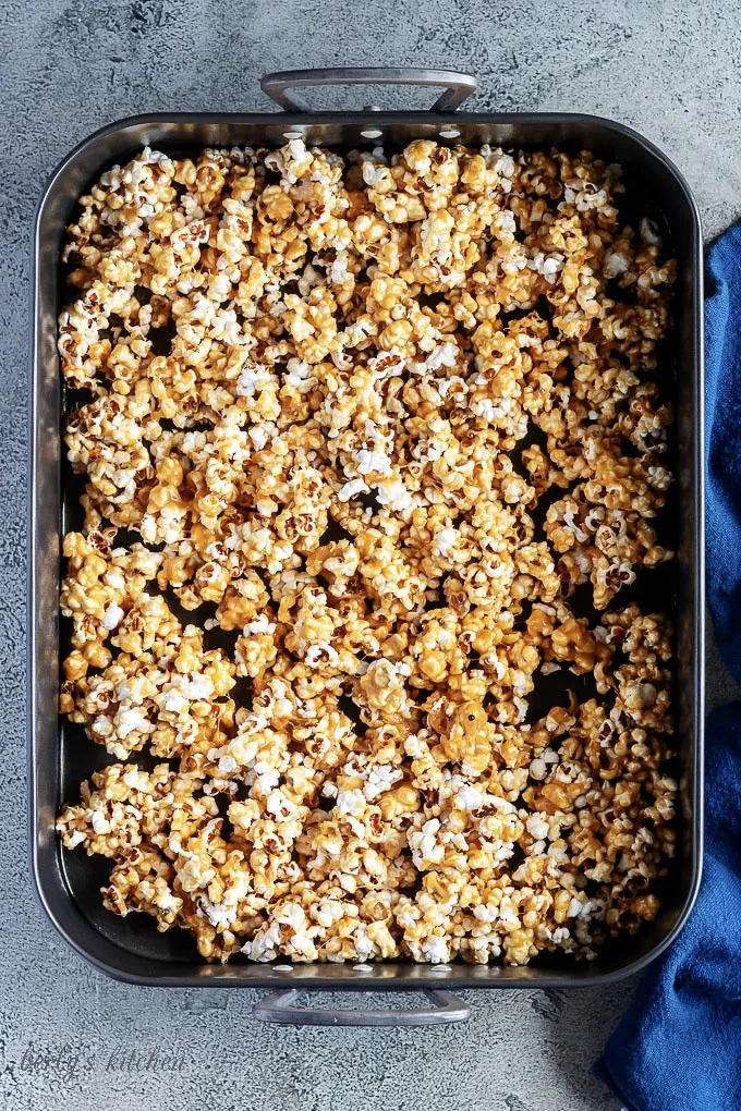 A top-down photo of the caramel corn popcorn spread out in a large roasting pan ready to be baked.