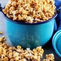 A close-up photo of the finished caramel corn served in a blue metal kettle with the popcorn overflowing the top of the pan.