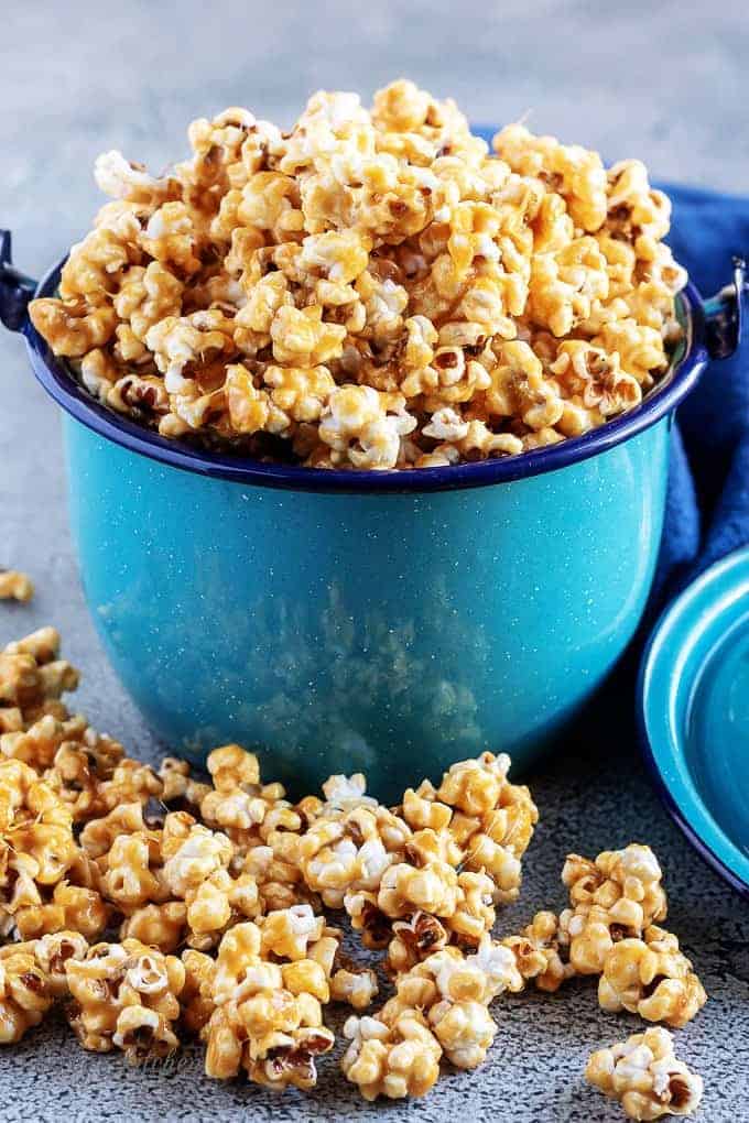 A close-up photo of the finished caramel corn served in a blue metal kettle with the popcorn overflowing the top of the pan.