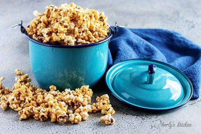 The finished caramel corn popcorn served in a blue kettle, spilling over the top of the kettle.