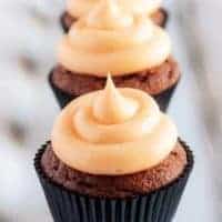 The cream cheese frosting topped cupcakes lined up in a row on a square plate.