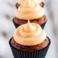 The cream cheese frosting topped cupcakes lined up in a row on a square plate.