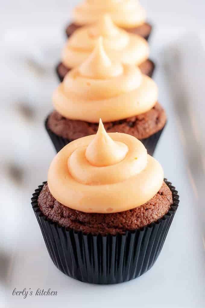 The cream cheese frosting topped cupcakes lined up in a row on a square plate.