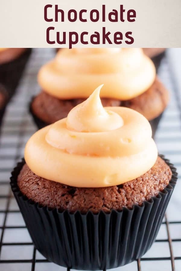 A large close-up photo of the chocolate cupcakes with orange frosting sitting in black cupcake liners.