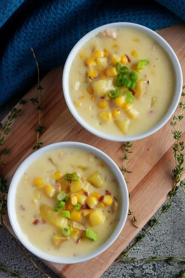 Photo looking down at the corn chowder with bacon, served in white bowls, topped with green onions.