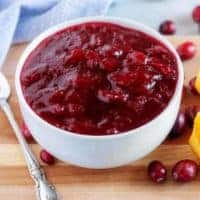 The final picture of the sauce in a white serving bowl surrounded by cranberries and orange wedges.