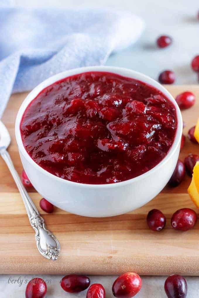 The final picture of the sauce in a white serving bowl surrounded by cranberries and orange wedges.