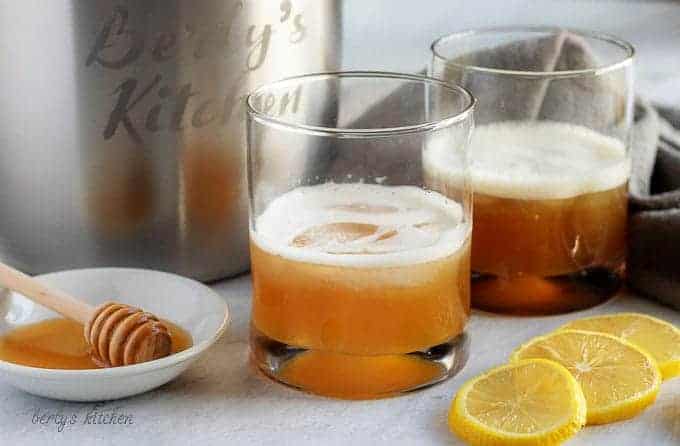 Two gold rush cocktails sitting in a cocktail glasses surrounded by lemon slices and honey on a plate.