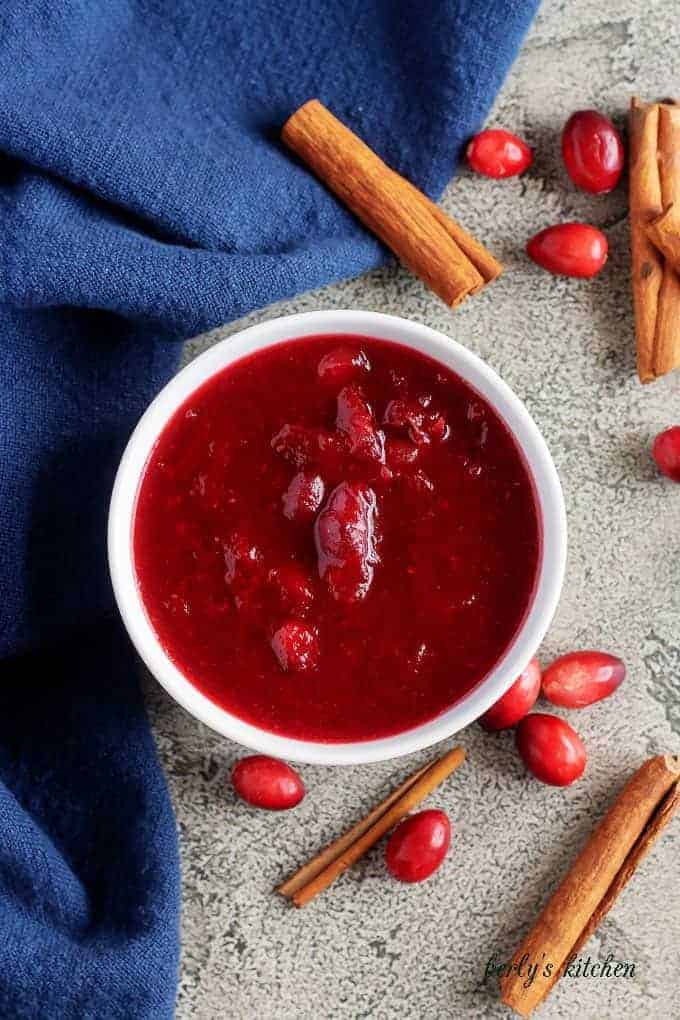 The last photo shows the finished homemade cranberry sauce in a bowl accented with cinnamon sticks.