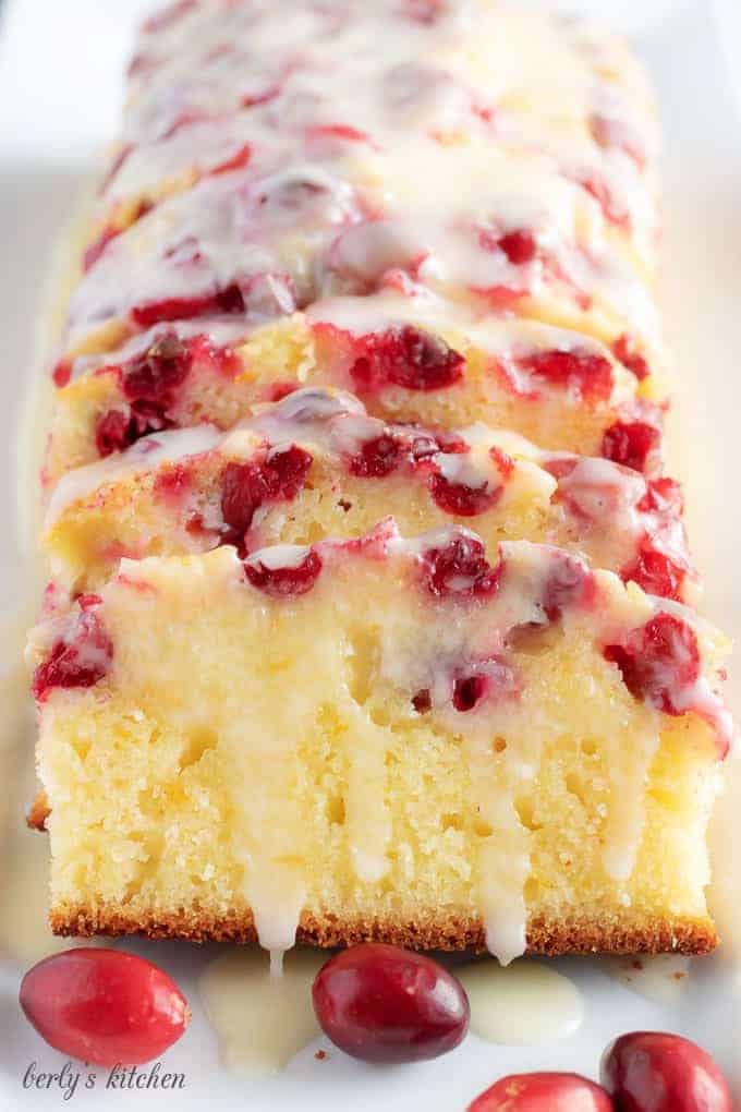 Baked and sliced loaf of orange cranberry bread drizzled with orange glaze.