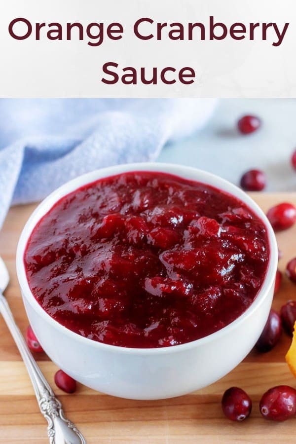 A large photo of the orange cranberry sauce, in a white bowl, surrounded by fresh cranberries.