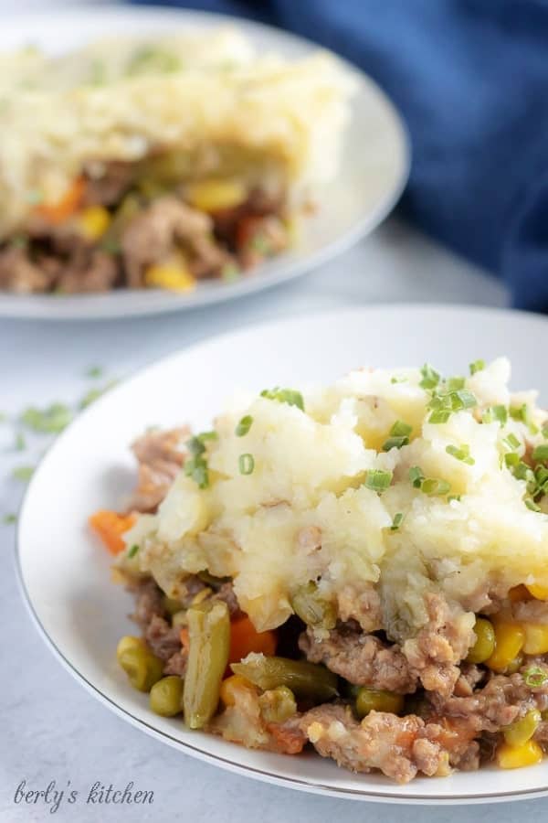 Another large picture of the finished shepherd's pie on a white plate, garnished with chives, and loaded with veggies and meat.