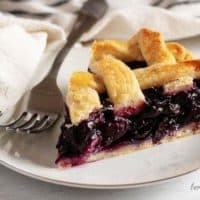 The finished blueberry pie recipe with a slice of pie sitting on a white plate.