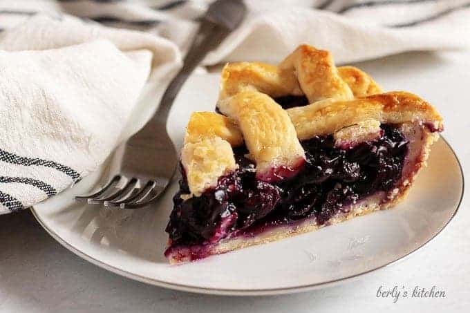 The finished blueberry pie recipe with a slice of pie sitting on a white plate.