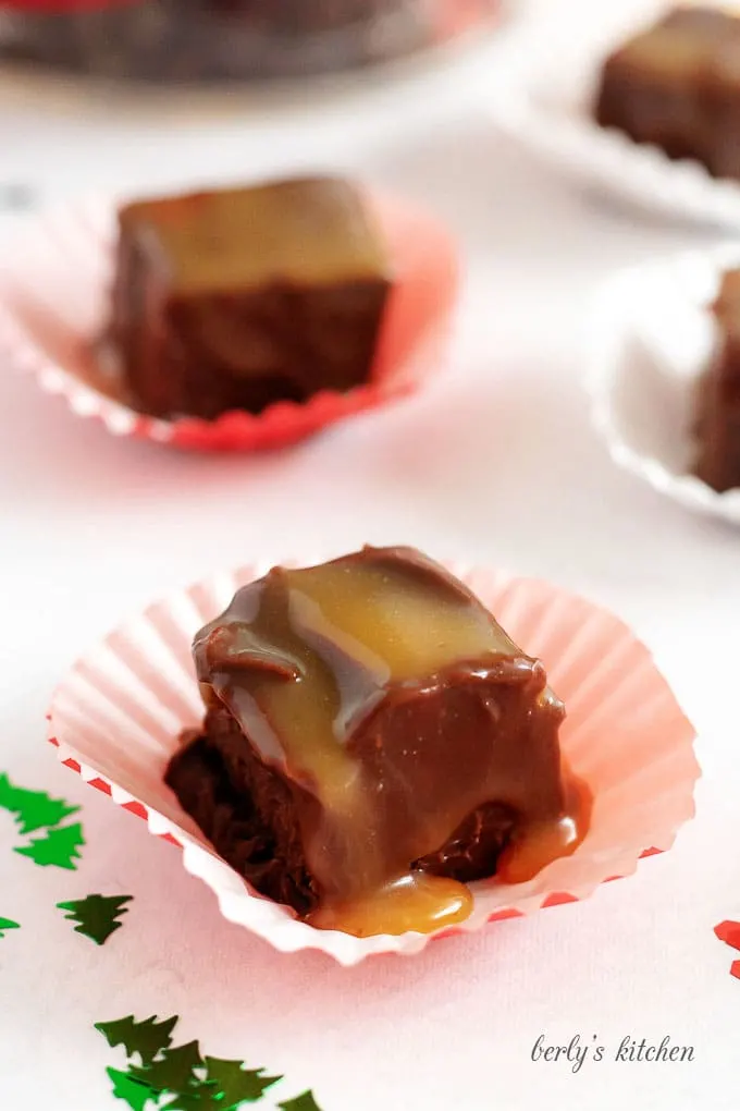 Pieces of bourbon caramel fudge in wrappers next to holiday confetti.