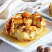 The finished bread pudding, topped with the rum sauce, sitting on a square plate.