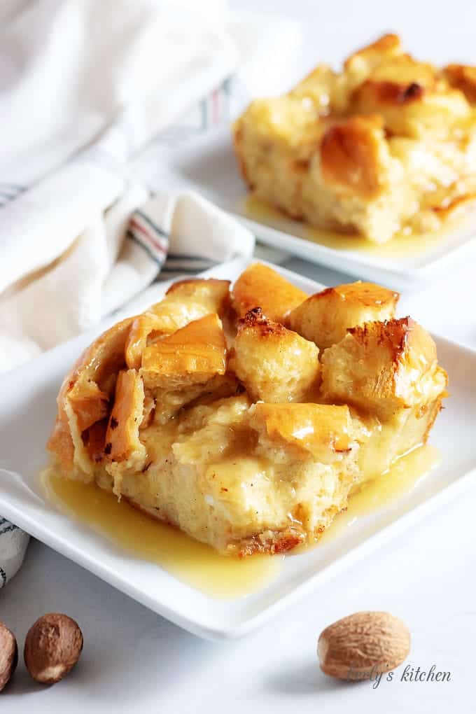 Two pieces of the bread pudding have been placed on square plates and topped with rum sauce.